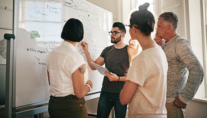 Team collaborating at a whiteboard to analyze processes, illustrating data visibility in logistics for smarter business decisions.