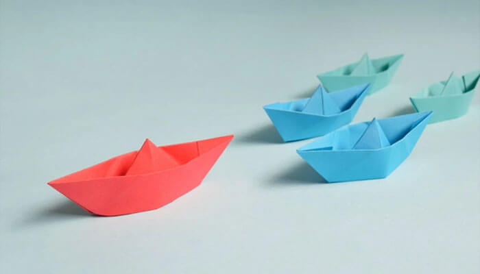 Paper boats in different colors, with a red boat leading the group, symbolizing the concept of a leadership mindset and effective leadership guiding others.