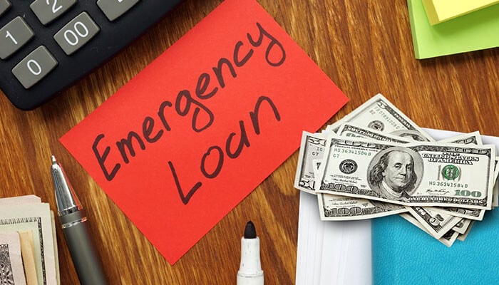 A desk with cash, a calculator, pen, and a red card labeled Emergency Loan representing urgent financial needs and relevant affiliate offers for cold traffic