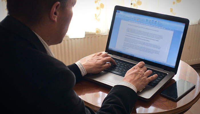 How Essay Writing Services Help Student Entrepreneurs - Startupeditor | Startup Editor A student entrepreneur typing on a laptop, working on business-related content or assignments, with a mobile phone on the table beside them.