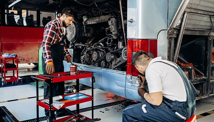 Maintenance Contractors - Startupeditor | Startup Editor Bus maintenance workers repairing engine and body parts, highlighting how poor upkeep can lead to mechanical failures and raise Bus Accident Liability issues.