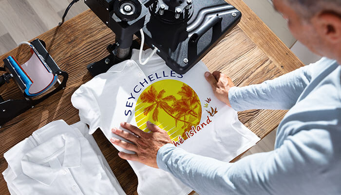 Minimalist and Clean Designs - Startupeditor | Startup Editor trends in t-shirt printing person heat-pressing a colorful Seychelles palm design onto a white T-shirt on a wooden table