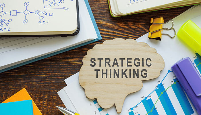 Practice Strategic Thinking - Startupeditor | Startup Editor Strategic thinking concept with the text STRATEGIC THINKING on a wooden brain icon surrounded by notes, charts, and office supplies, symbolizing the development of a leadership mindset.
