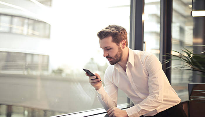 A businessman in a white shirt looking at his phone, symbolizing the preparation and strategic thinking involved in transitioning from side hustle to business