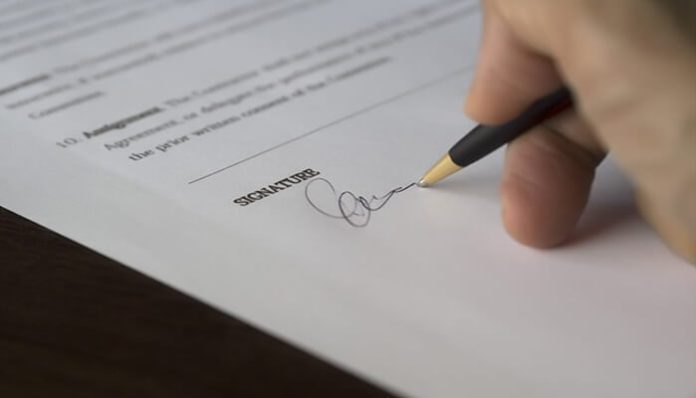 Close-up of a hand signing a legal document, symbolizing commitment and due diligence required when investing in business insurance.