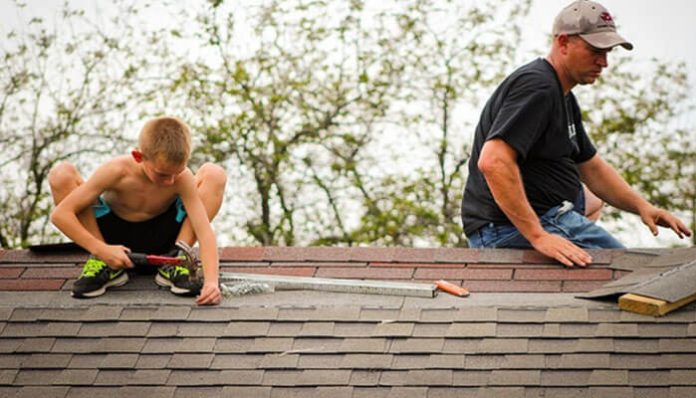 Father and son repairing shingles on a roof while doing seasonal maintenance, showing the risks of DIY projects and common roofing mistakes.