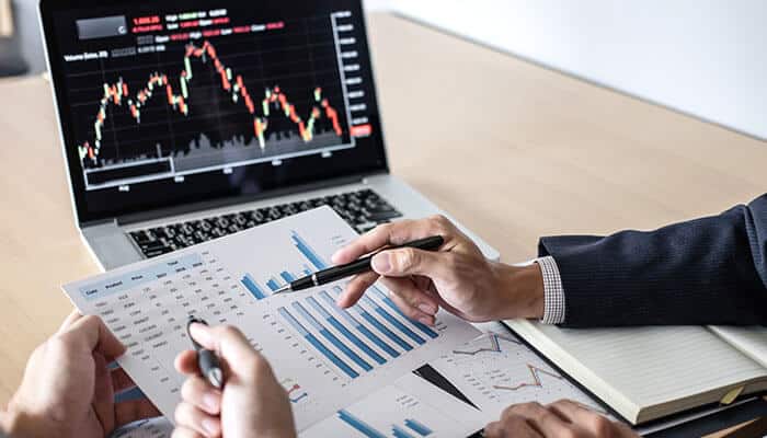 Funded traders strategies discussed with charts and graphs, analyzing financial data alongside a laptop showing market trends for risk and profit planning.