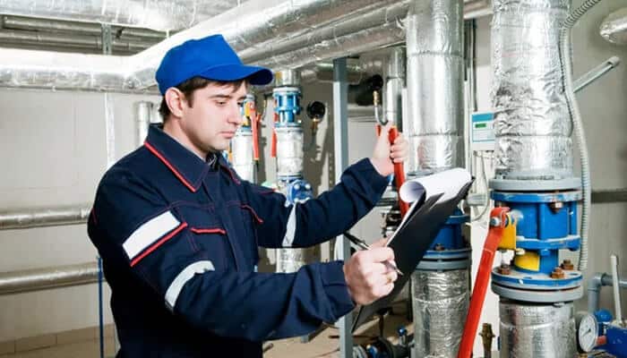 Technician inspecting boiler supplies and components in a commercial boiler room, ensuring proper system functioning and safety.
