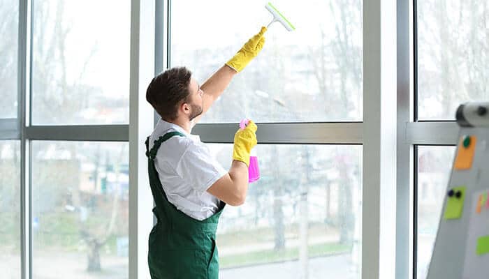 Easy Everyday Cleaning - Startupeditor | Startup Editor Worker cleaning large glass panels of uPVC windows low-maintenance design with spray and squeegee.