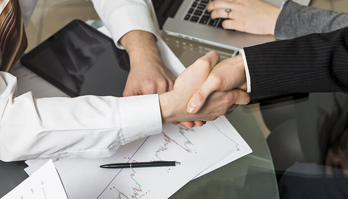 Two business professionals shaking hands over financial documents and a laptop, symbolizing agreement and resolution in Shareholder Disputes.