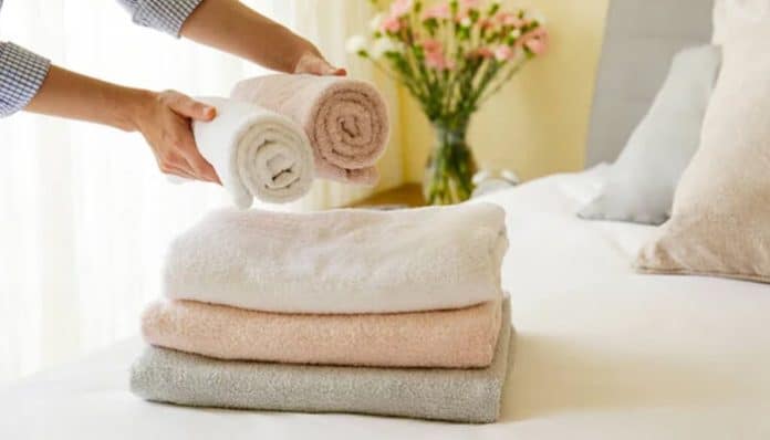 Person folding soft organic cotton hand towels in a calm, cozy bedroom setting, demonstrating their comfort and sustainable appeal.