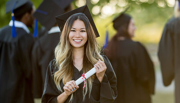 Smiling graduate holding a diploma during commencement ceremony, symbolizing achievement and the importance of diploma verification in careers.