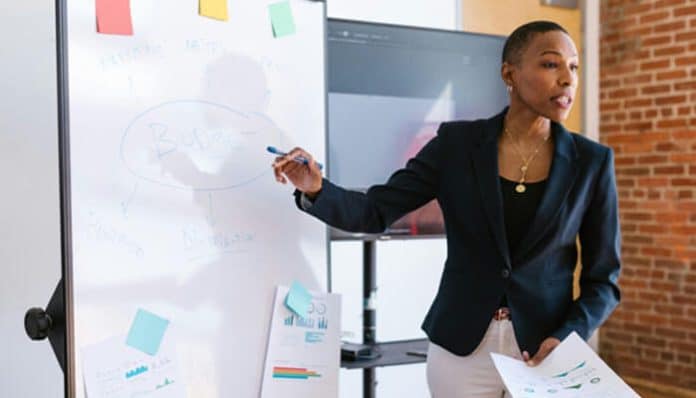 A professional woman presenting a budget plan on a whiteboard with financial charts in the background. This image highlights the significance of strategic financial planning for startups, focusing on managing startup finances to ensure growth and success.