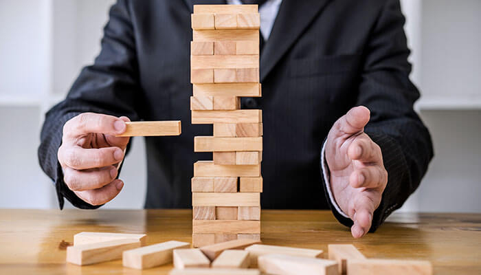 Reframing Risk as a Strategic Advantage - Startupeditor | Startup Editor Businessman balancing wooden blocks like a tower game, symbolizing startup scaling priorities, risk management, and stability in growth