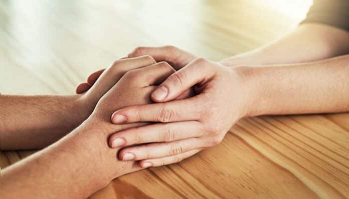 Hands gently holding each other on a wooden table, symbolizing compassion, care, and the power of an act of kindness.