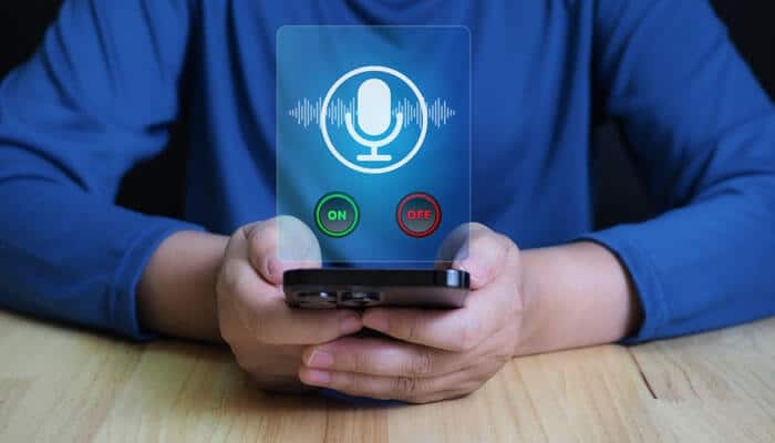 Person using a smartphone with a holographic microphone icon and on/off buttons, illustrating the use of AI voice assistants and voice-enabled technology
