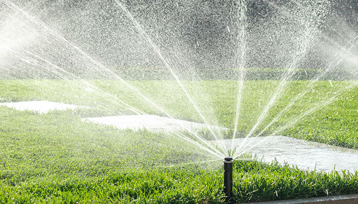 Sprinkler system watering the lawn, potentially highlighting hidden water troubles in the yard such as uneven moisture distribution and water seepage issues.