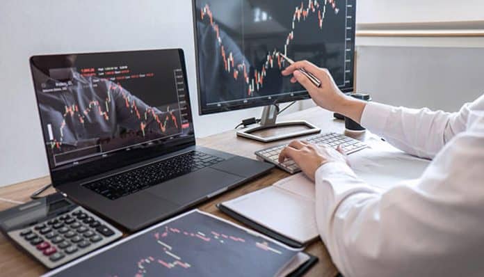 Compliance and Security in Trading Platforms shown by trader analyzing financial charts on laptop and monitors with secure trading systems