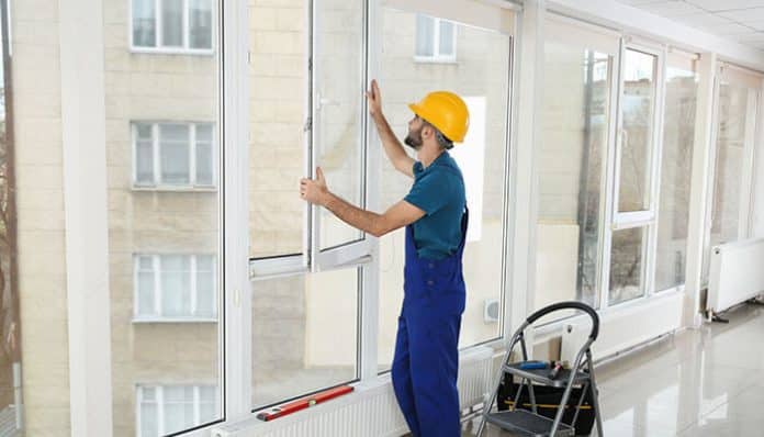 Professional installer fitting a glass window panel in a modern building, wearing safety gear and helmet — illustrating double glazing installation for energy efficiency.