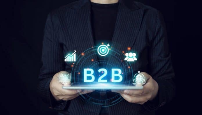 A business professional holds a digital tablet displaying the glowing word B2B, surrounded by icons representing analytics, customer engagement, and marketing strategy, symbolizing B2B sales success and the customer journey