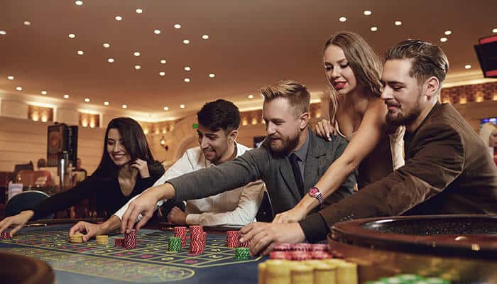Group of friends playing roulette at a casino table, placing colorful chips and smiling under warm lights — representing social gaming and casino bonuses excitement.