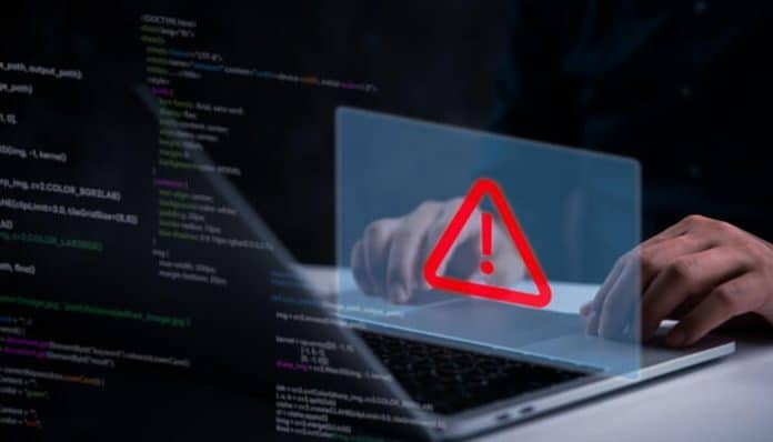 A person typing on a laptop displaying a red warning icon, representing cyberattacks and common threats that affect businesses like phishing and ransomware.