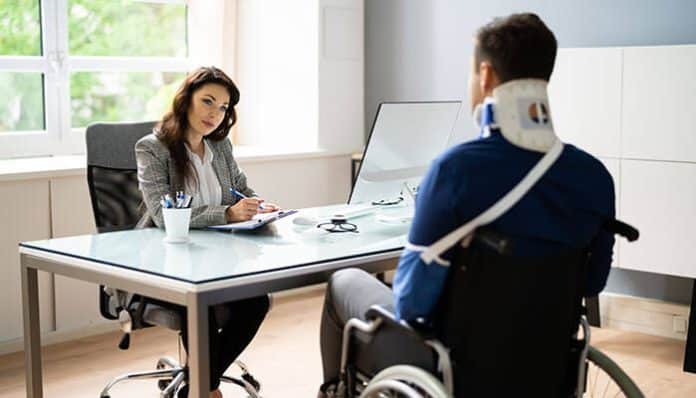 An injured man in a wheelchair with a neck brace speaks to a lawyer in an office, representing legal consultation to prove liability in a personal injury case