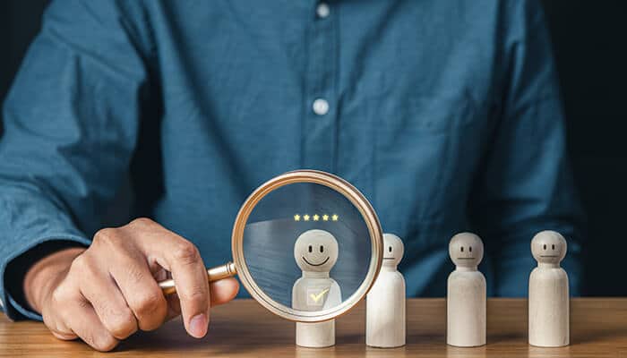 Magnifying glass highlighting a smiling candidate among wooden figures, symbolizing Best Recruiters for Organizational Growth in selecting top talent.