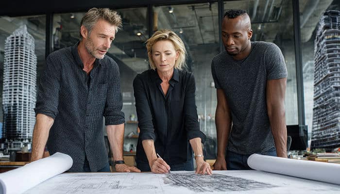 A team of IT and security professionals collaborating over network architecture blueprints, discussing how cybercriminals exploit system vulnerabilities and security gaps