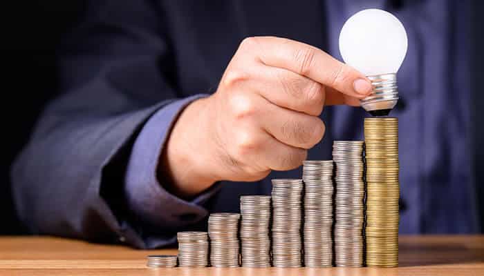 A person stacking coins in ascending order with a glowing light bulb on top, symbolizing creative ideas, planning and transformation, representing how to turn a messy garage into a space that is organized, efficient and functional.