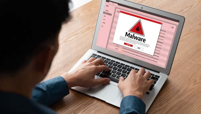 A person using a laptop showing a malware warning screen, symbolizing common threats that affect businesses such as viruses, ransomware, and cybersecurity risks.