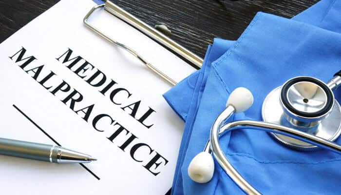 Document labeled medical malpractice placed beside a stethoscope and blue scrubs representing awareness about common causes of personal injuries.