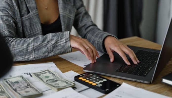 A financial professional analyzing reports and managing accounts on a laptop with cash and calculator on desk showing strong finance skills under pressure.