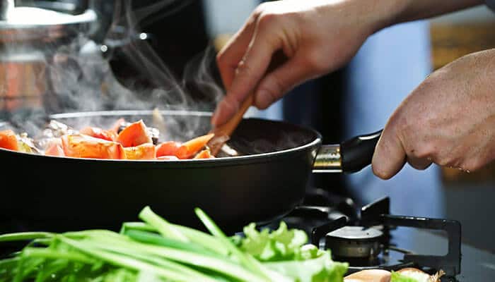 Person cooking fresh vegetables in a pan on the stove, highlighting simple cooking methods that support Wholesome Eating and natural flavors.