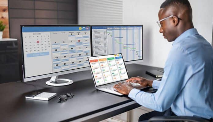 A man is working on a computer with multiple screens displaying a volunteer management software dashboard, showing scheduling tools, task tracking, and volunteer coordination features for efficient management.