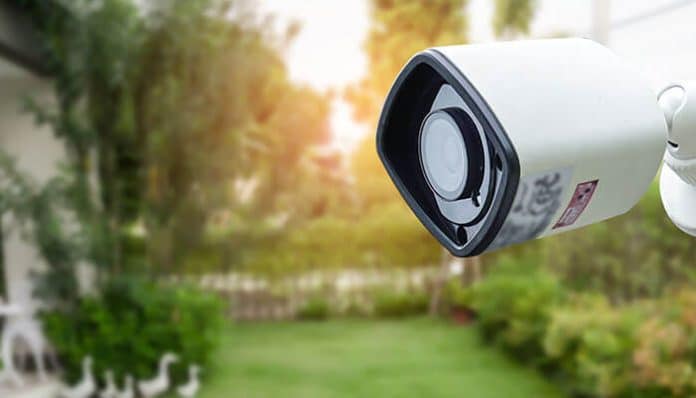 A white CCTV camera mounted outside a home overlooking a green garden, symbolizing safety, surveillance, and modern CCTV home security solutions for residential protection.
