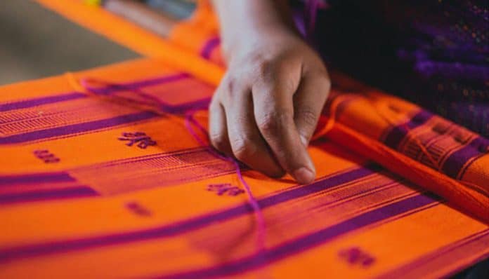 A close-up of a craftsman weaving vibrant orange and purple fabric by hand, symbolizing traditional craftsmanship, sustainability, and the values upheld by ethical clothing manufacturers