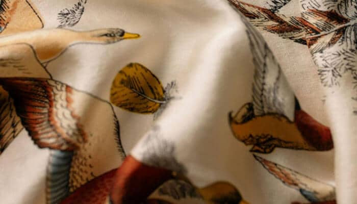 Close-up of soft, patterned fabric featuring elegant bird and leaf designs, representing sustainable materials and artistic quality promoted by ethical clothing manufacturers