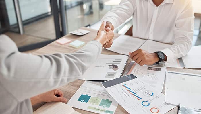Business professionals shaking hands over analytics charts and reports, symbolizing successful partnerships powered by B2B marketing technology strategies.
