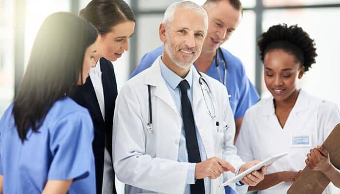 A senior doctor and healthcare team reviewing patient information together in a bright medical office, representing teamwork and collaboration in small practices staffing.