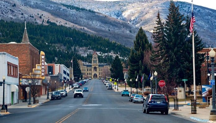 Downtown view of one of Montana’s cities with cars parked along a clean, walkable street, surrounded by trees and mountains in the background, highlighting sustainable urban living