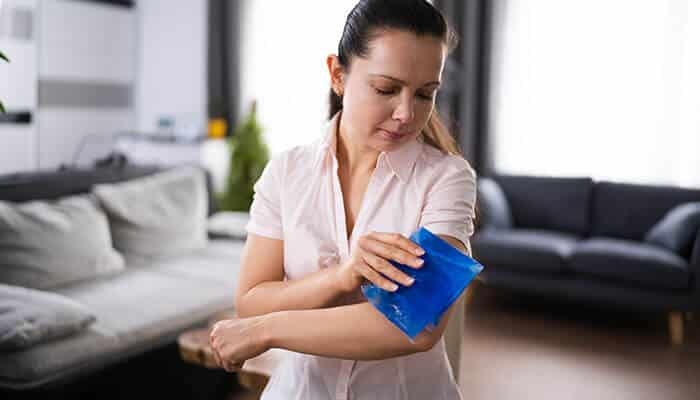 Woman applying an ice pack to her arm at home to minimize pain during tattoo removal recovery