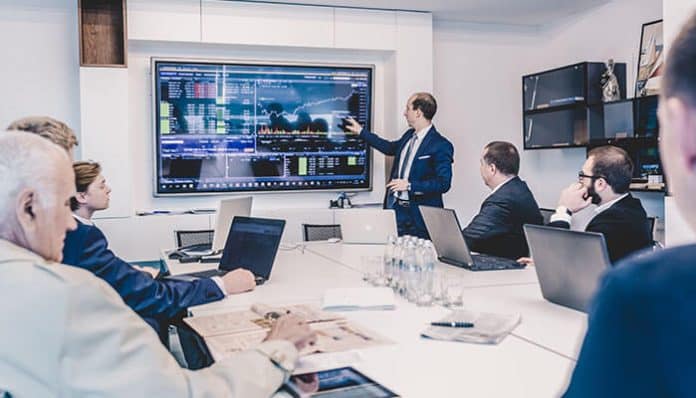A board meeting in session with executives reviewing data on a large digital screen, highlighting the efficiency offered by top board management software providers.