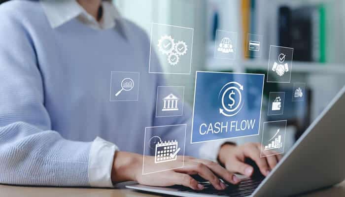 A person working on a laptop with digital icons showing cash flow and financial tools, representing hedges for small businesses to protect against market risks.