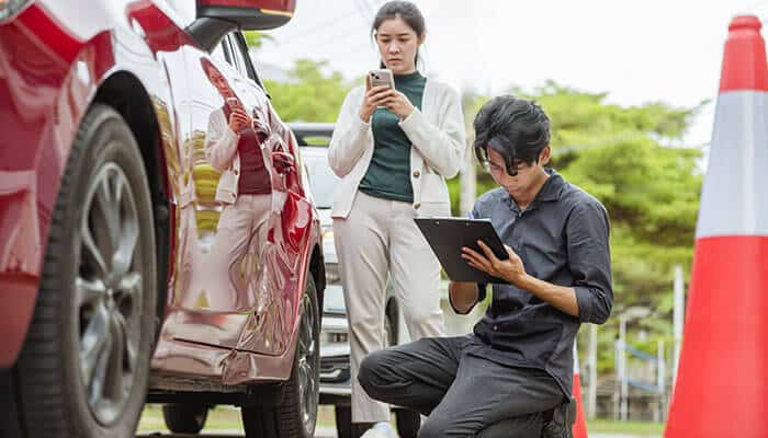 Insurance adjuster inspecting car damage while driver documents the crash, showing the need for legal guidance for car accident claims.