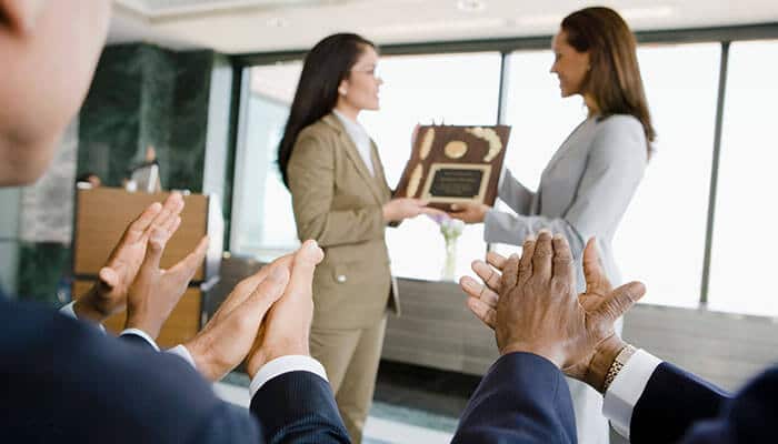 A businesswoman presenting a custom award plaque to a client, highlighting the importance of award ideas for clients in recognizing achievements and building relationships.