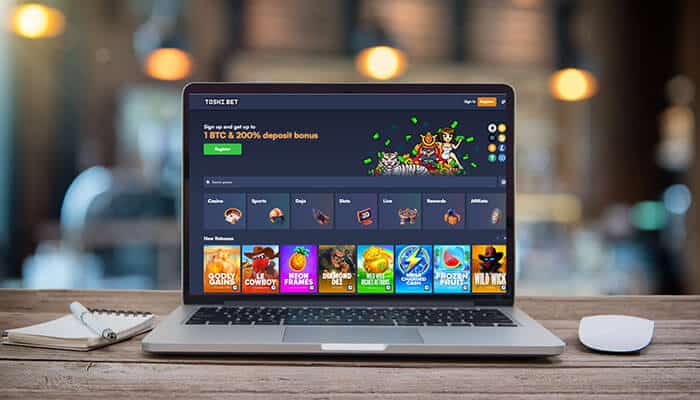A laptop displaying the Toshi.bet online casino interface with games and promotions on the screen.