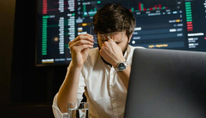 A stressed business owner looking at volatile market data on a screen, highlighting the need for hedges for small businesses to protect against financial risk.
