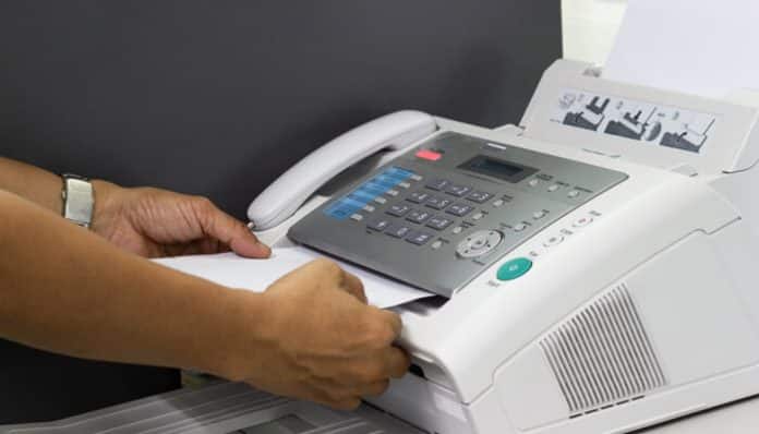 Person operating a traditional fax machine, highlighting the shift to online faxing software for faster business communication.