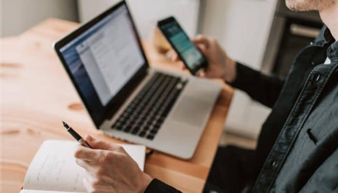 A hotel staff member using a laptop and smartphone to manage tasks, showing how smart technology in hospitality improves communication and operations.